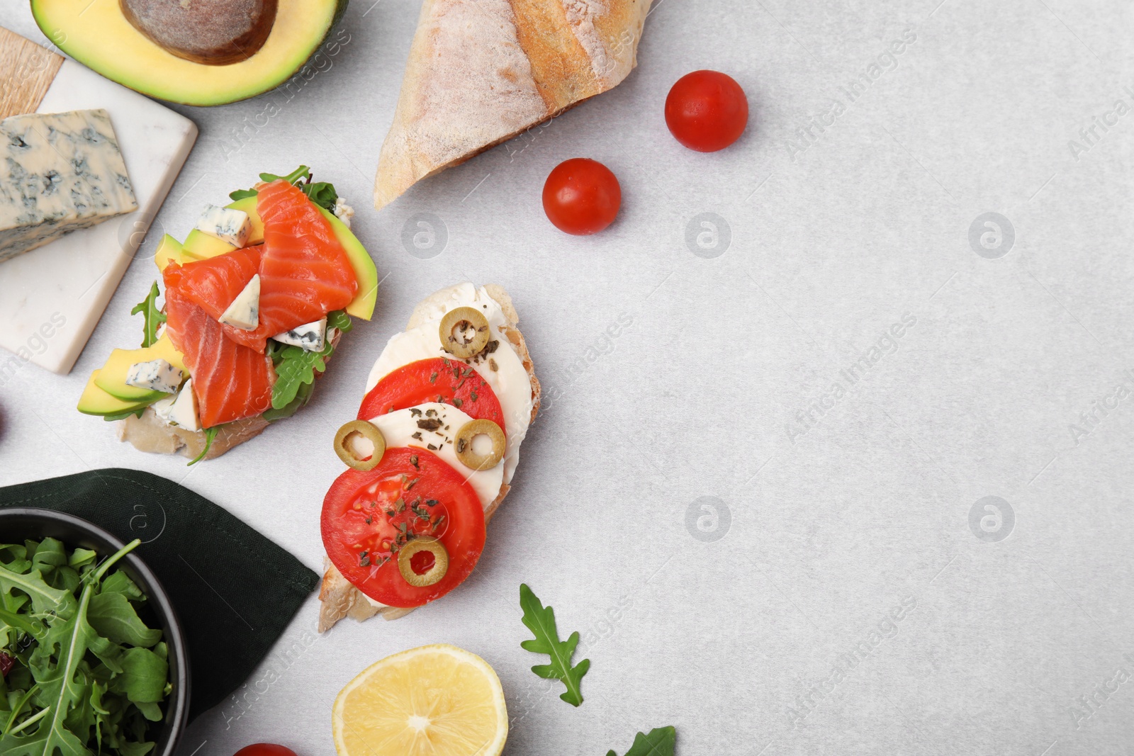 Photo of Flat lay composition with different tasty bruschettas and ingredients on light grey textured table. Space for text