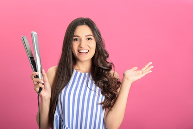 Photo of Young woman with modern hair iron on pink background, space for text