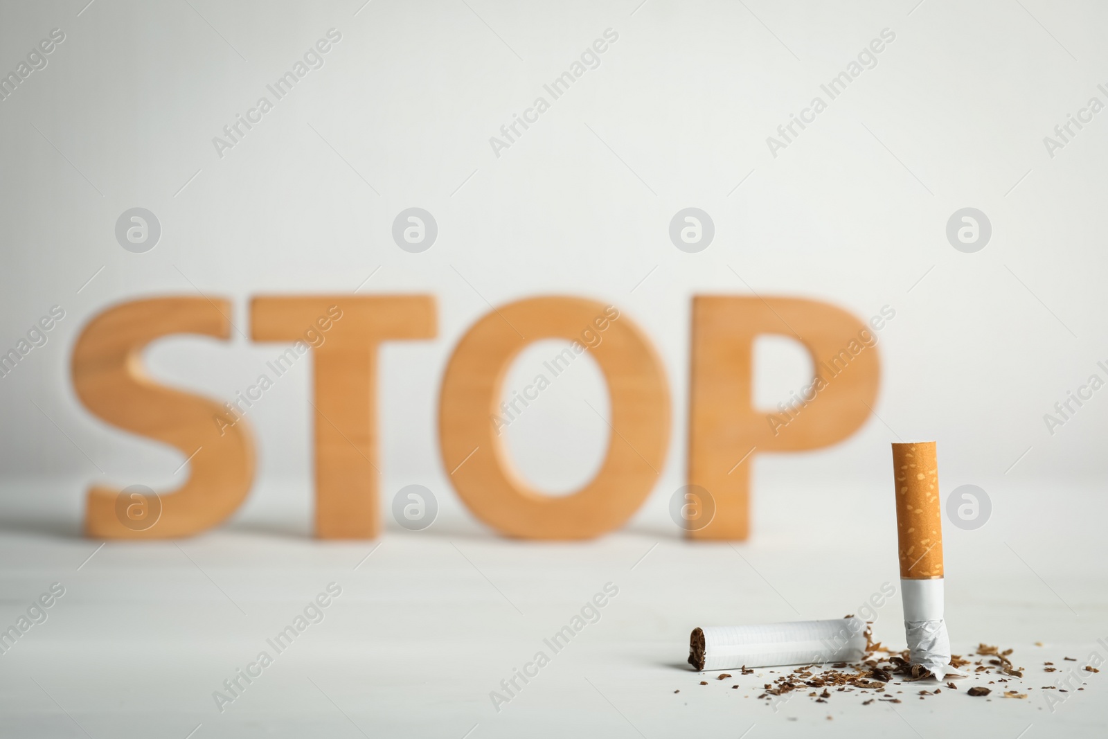Photo of Broken cigarette near word Stop on white table. Quitting smoking concept
