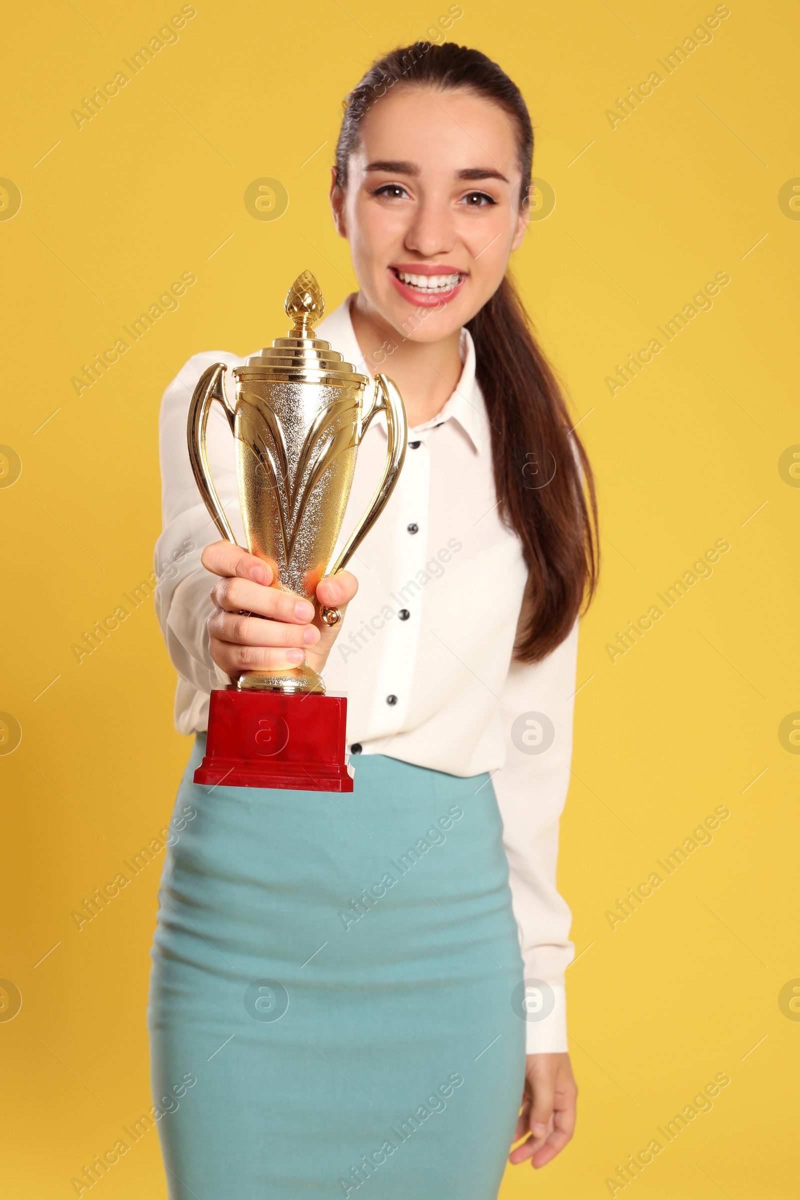 Photo of Portrait of happy young businesswoman with gold trophy cup on yellow background