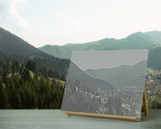 Image of Wooden easel with picture on table and beautiful mountain landscape 