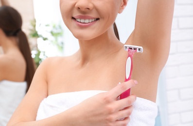 Photo of Beautiful young woman shaving armpit at home, closeup