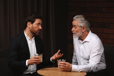 Photo of Men with glasses of whiskey talking at wooden table indoors