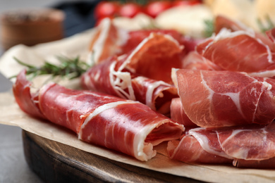 Photo of Slices of tasty prosciutto on grey table, closeup