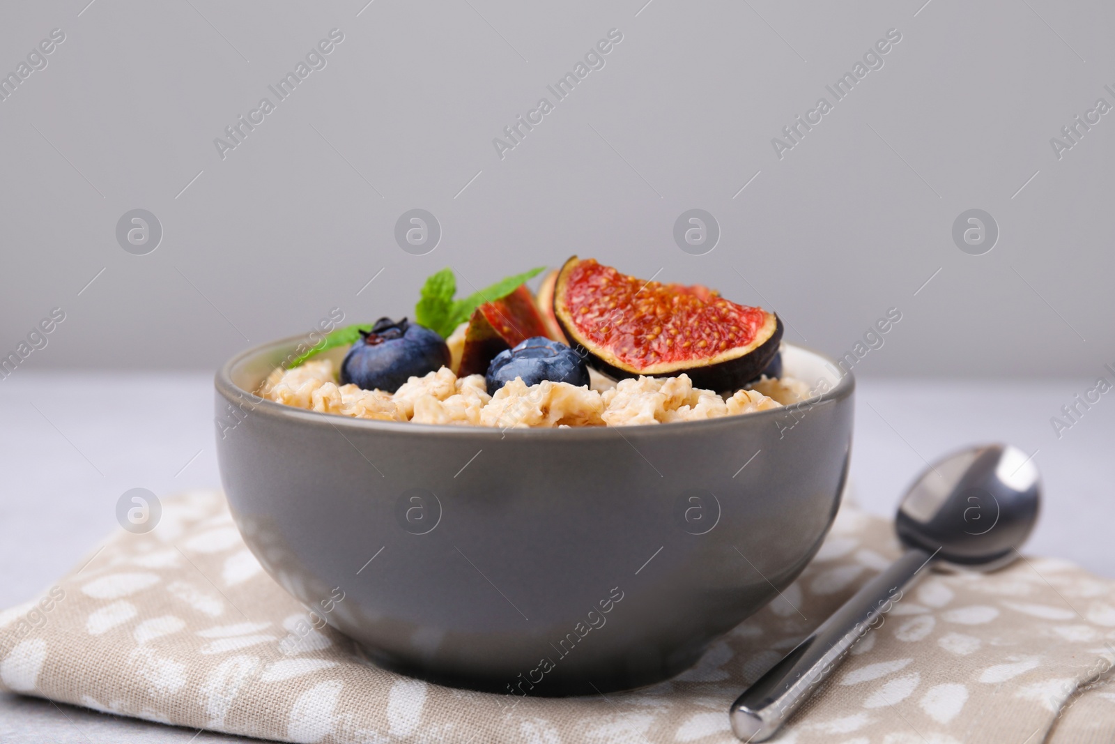 Photo of Oatmeal served with blueberries, mint and fig pieces on light grey table, closeup