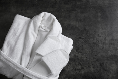 Photo of Clean folded bathrobe and slippers on black stone background, top view. Space for text