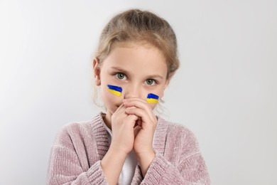 Little girl with drawings of Ukrainian flag on face against white background