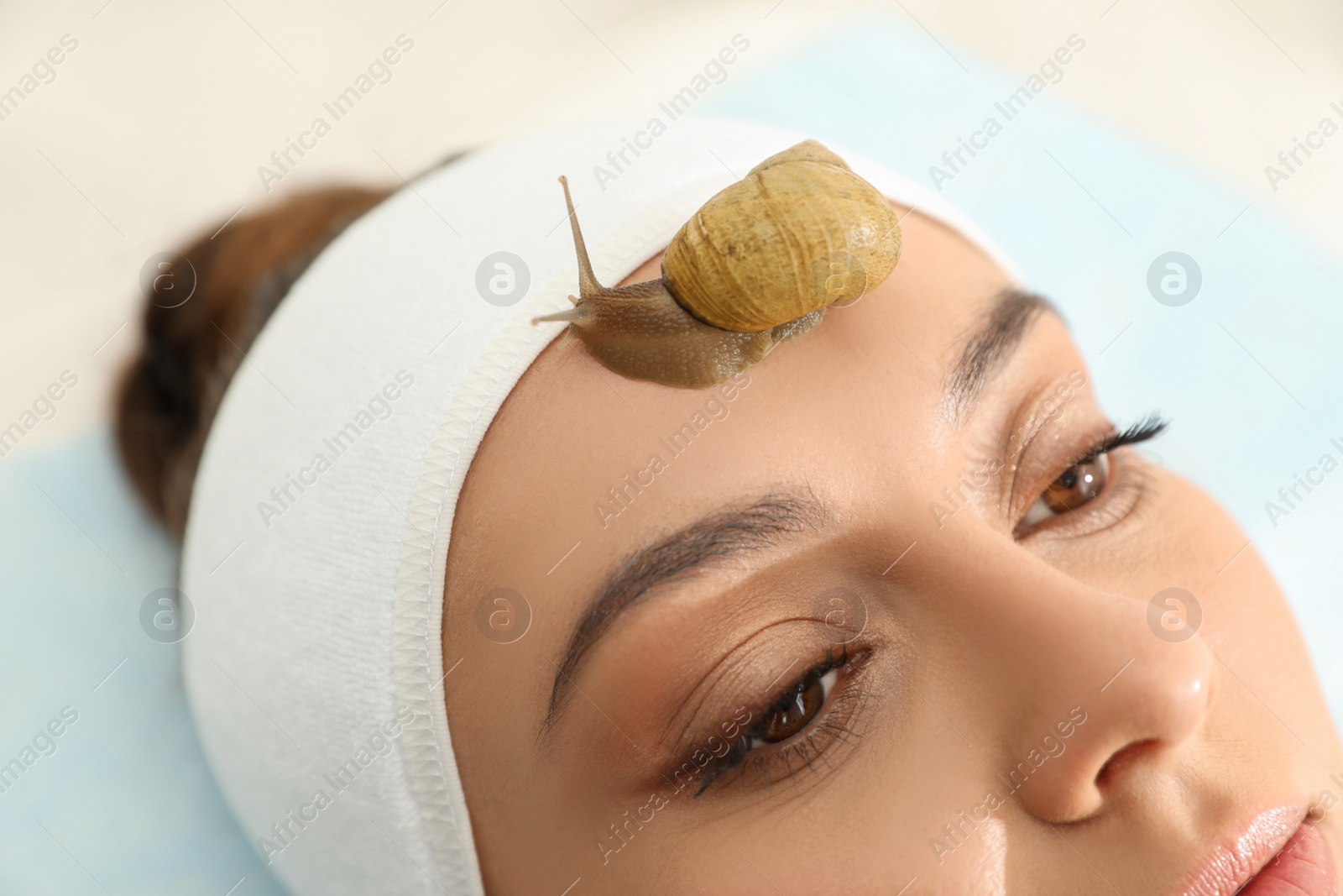 Photo of Young woman receiving snail facial massage in spa salon, closeup