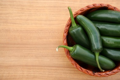 Bowl of fresh green jalapeno peppers on wooden table, top view. Space for text