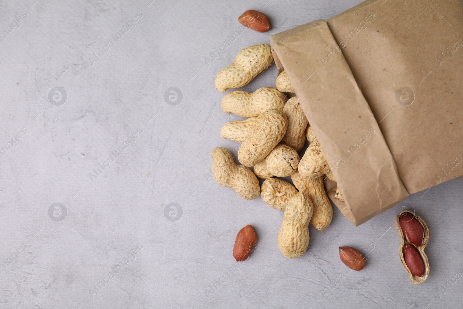 Photo of Paper bag with fresh unpeeled peanuts on grey table, top view. Space for text