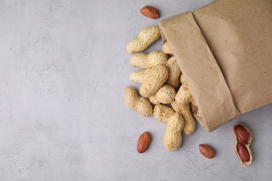 Paper bag with fresh unpeeled peanuts on grey table, top view. Space for text