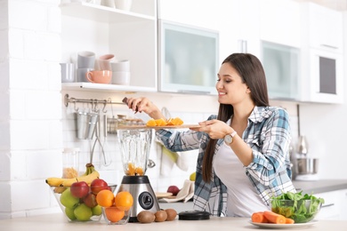 Photo of Young woman preparing tasty healthy smoothie at table in kitchen