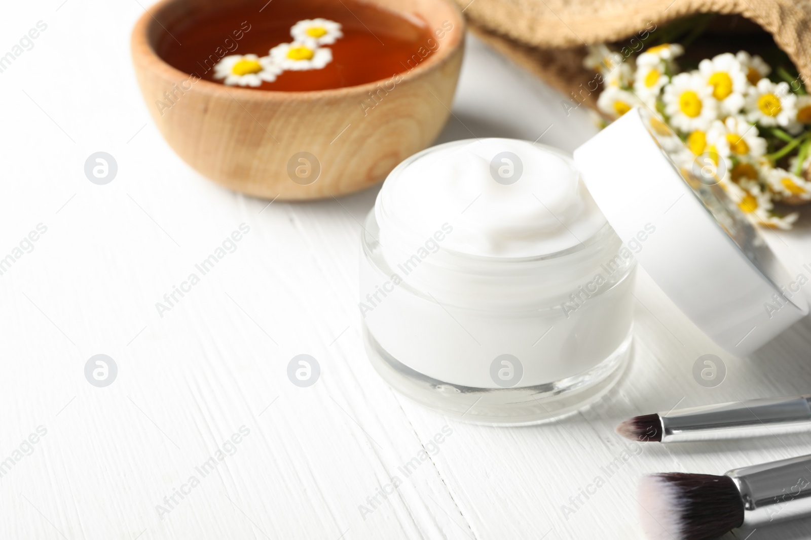 Photo of Jar of cream, brushes and chamomiles on white wooden table