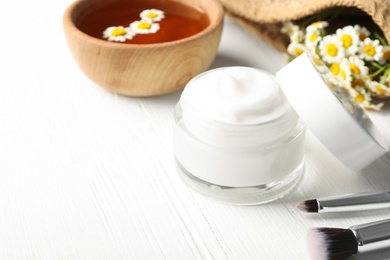 Jar of cream, brushes and chamomiles on white wooden table