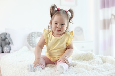 Adorable little baby girl sitting on bed in room