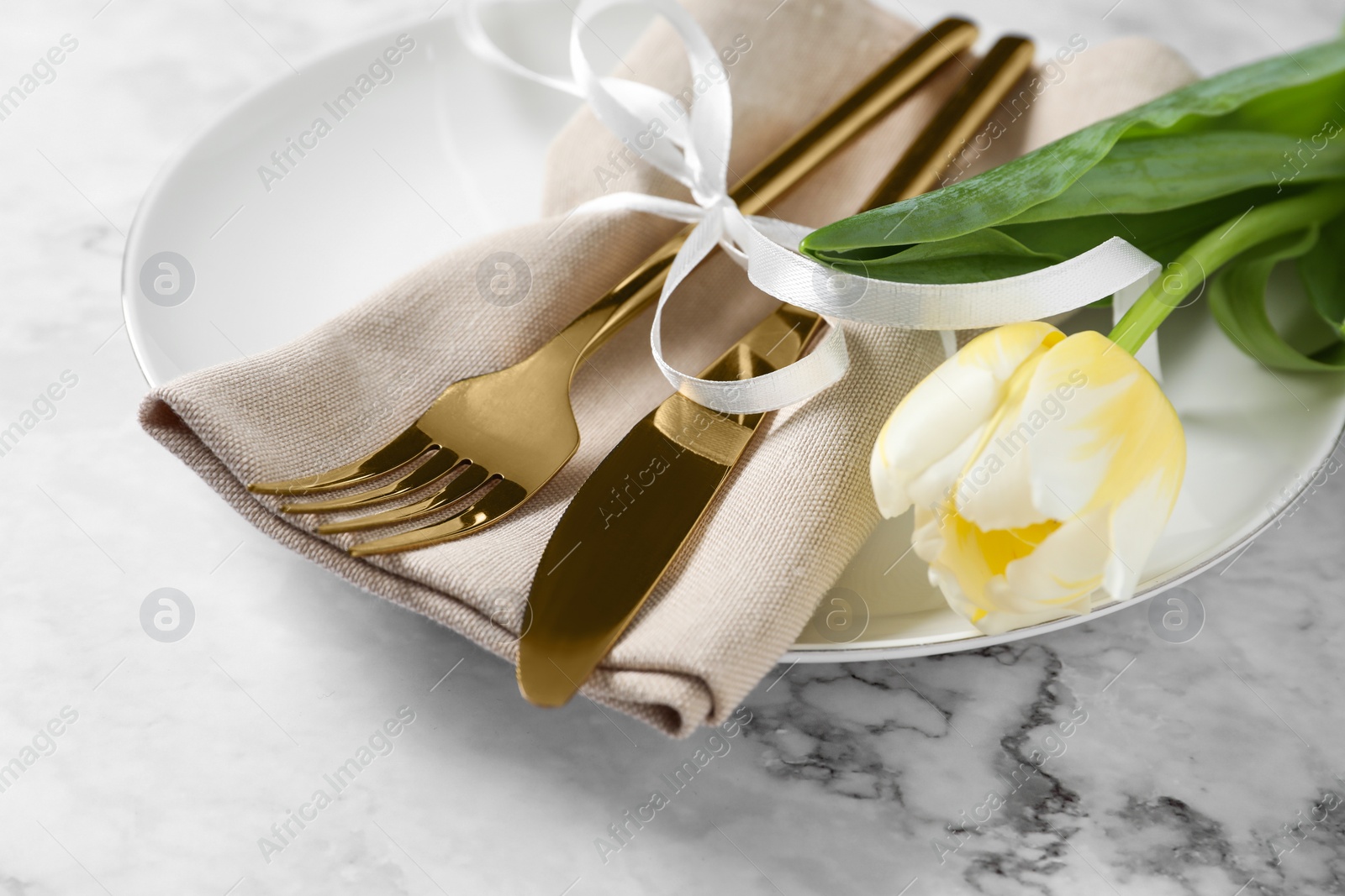 Photo of Stylish table setting with cutlery and tulip on white marble background, closeup