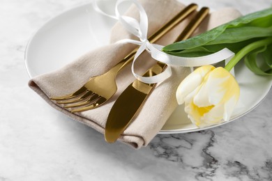 Photo of Stylish table setting with cutlery and tulip on white marble background, closeup