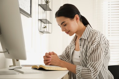 Photo of Beautiful young woman praying over Bible at desk