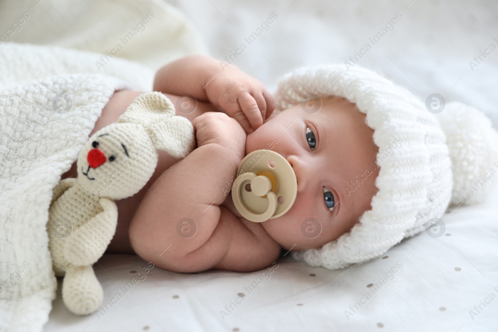 Photo of Cute newborn baby in white knitted hat lying on bed