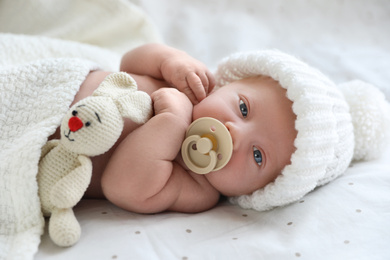 Cute newborn baby in white knitted hat lying on bed