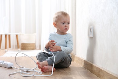 Photo of Little child playing with power strip plug near electrical socket at home. Dangerous situation