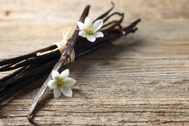 Photo of Bunch of vanilla pods and flowers on wooden table, closeup. Space for text