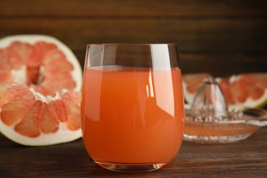 Photo of Glass of pink pomelo juice and fruit on wooden table, closeup