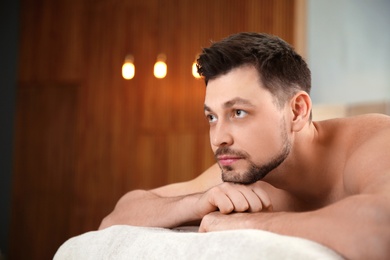 Photo of Handsome man relaxing on massage table in spa salon. Space for text