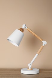 Photo of Stylish modern desk lamp on wooden table near beige wall