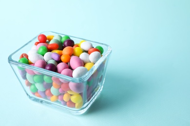 Yummy candies in glass bowl on light blue background, space for text