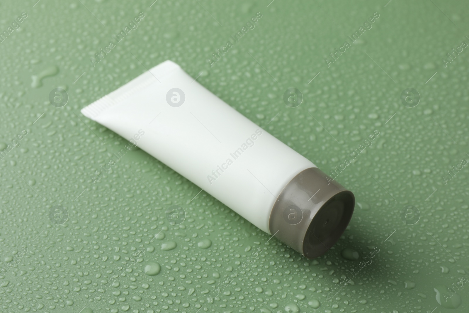 Photo of Moisturizing cream in tube on green background with water drops, closeup