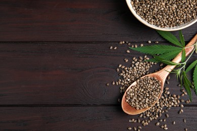 Photo of Organic hemp seeds and leaves on wooden table, flat lay. Space for text