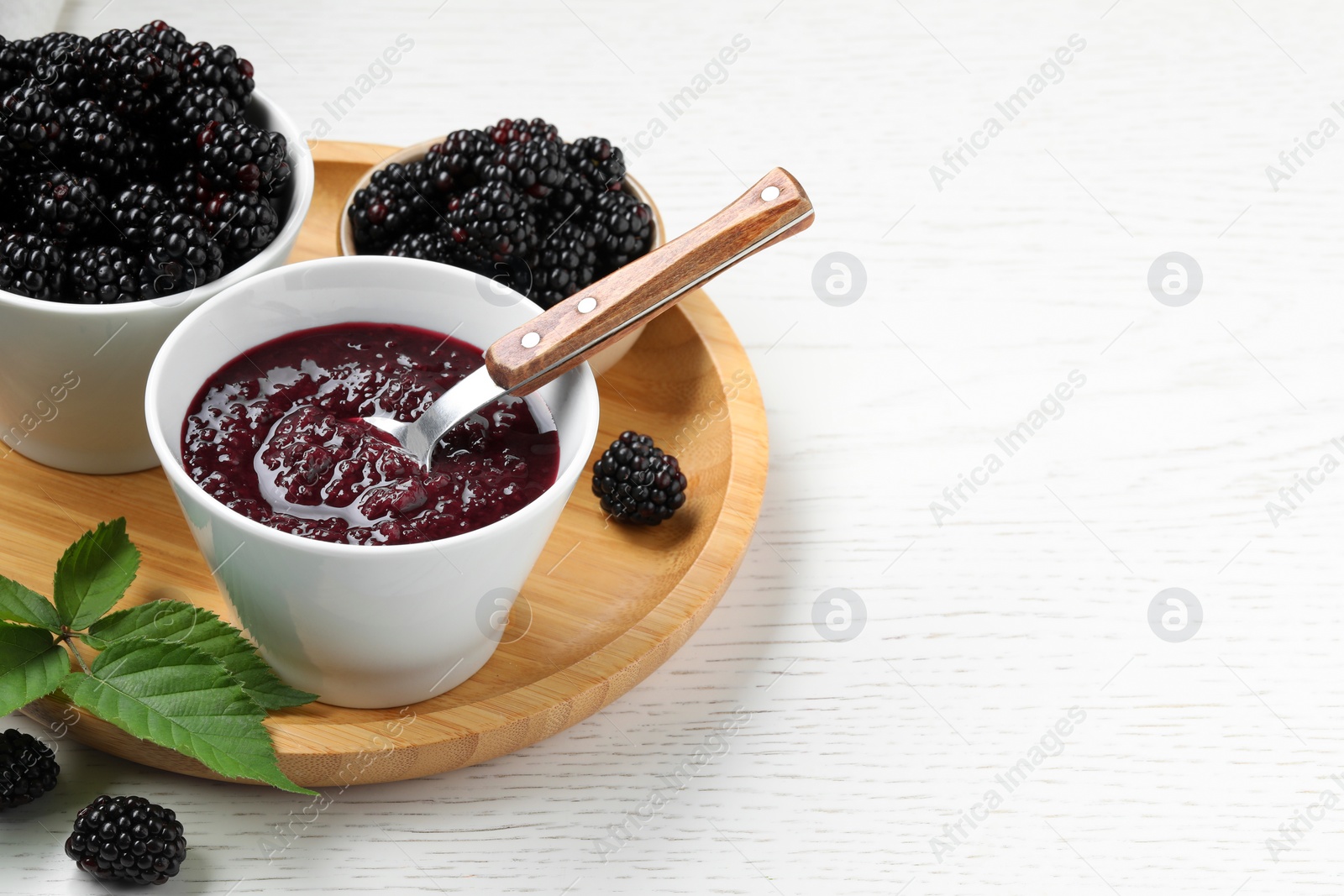 Photo of Fresh ripe blackberries, tasty jam and leaves on white wooden table, closeup. Space for text