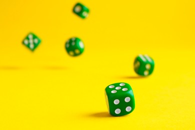 Many green game dices falling on yellow background, closeup