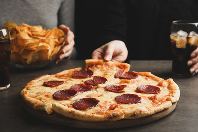Photo of Woman taking tasty pepperoni pizza at grey table, closeup