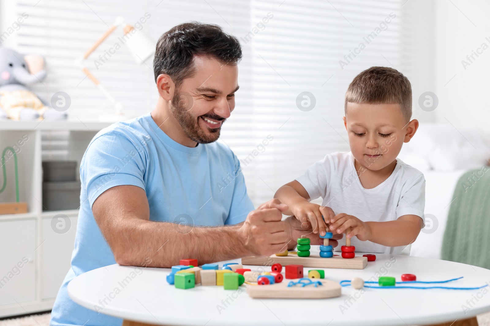 Photo of Motor skills development. Father and his son playing with stacking and counting game at table indoors