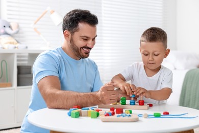 Photo of Motor skills development. Father and his son playing with stacking and counting game at table indoors