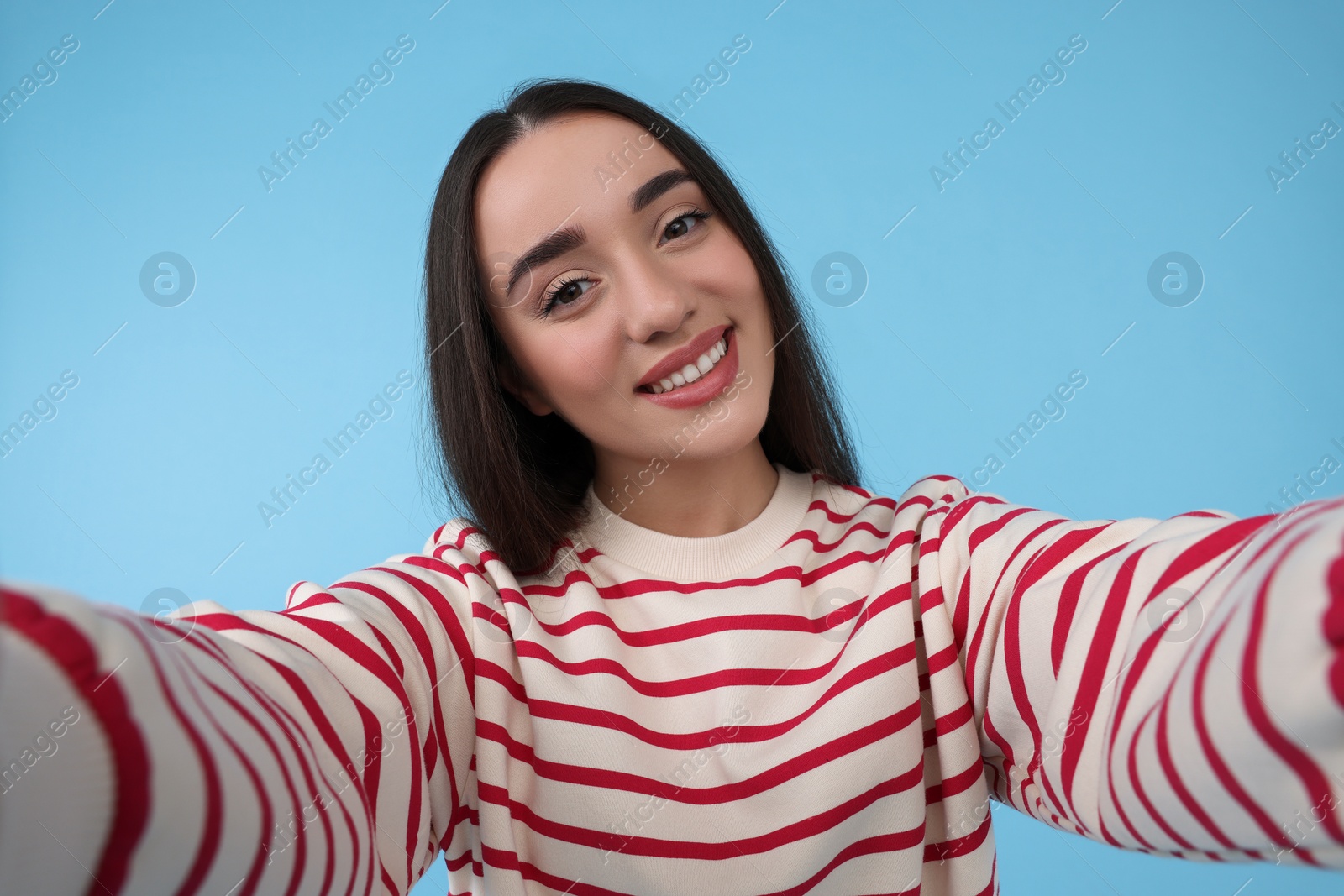 Photo of Smiling young woman taking selfie on light blue background