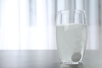 Glass with effervescent tablet on grey table indoors, space for text. Medical care