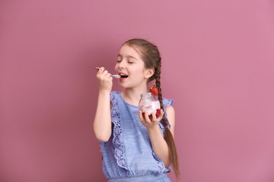 Photo of Cute girl eating tasty yogurt on color background