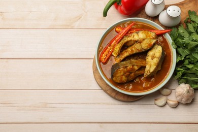 Tasty fish curry and ingredients on white wooden table, flat lay. Space for text. Indian cuisine