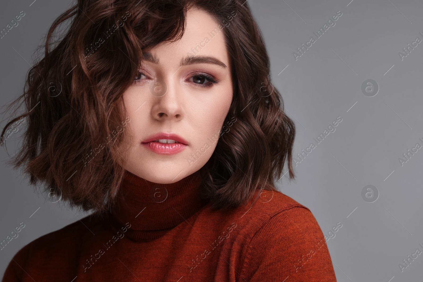 Photo of Portrait of beautiful young woman with wavy hairstyle on grey background. Space for text