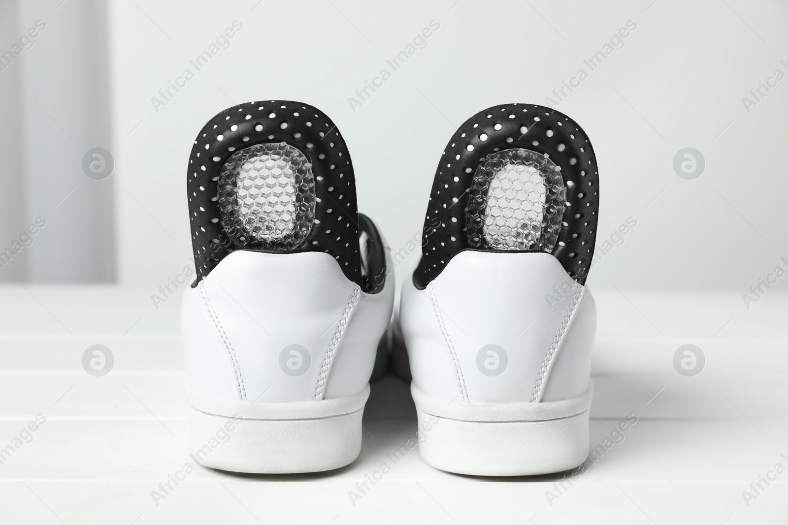 Photo of Orthopedic insoles in shoes on white wooden floor, closeup
