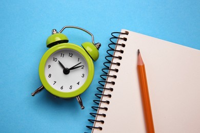 Alarm clock, pencil and notebook on light blue background, flat lay. Reminder concept