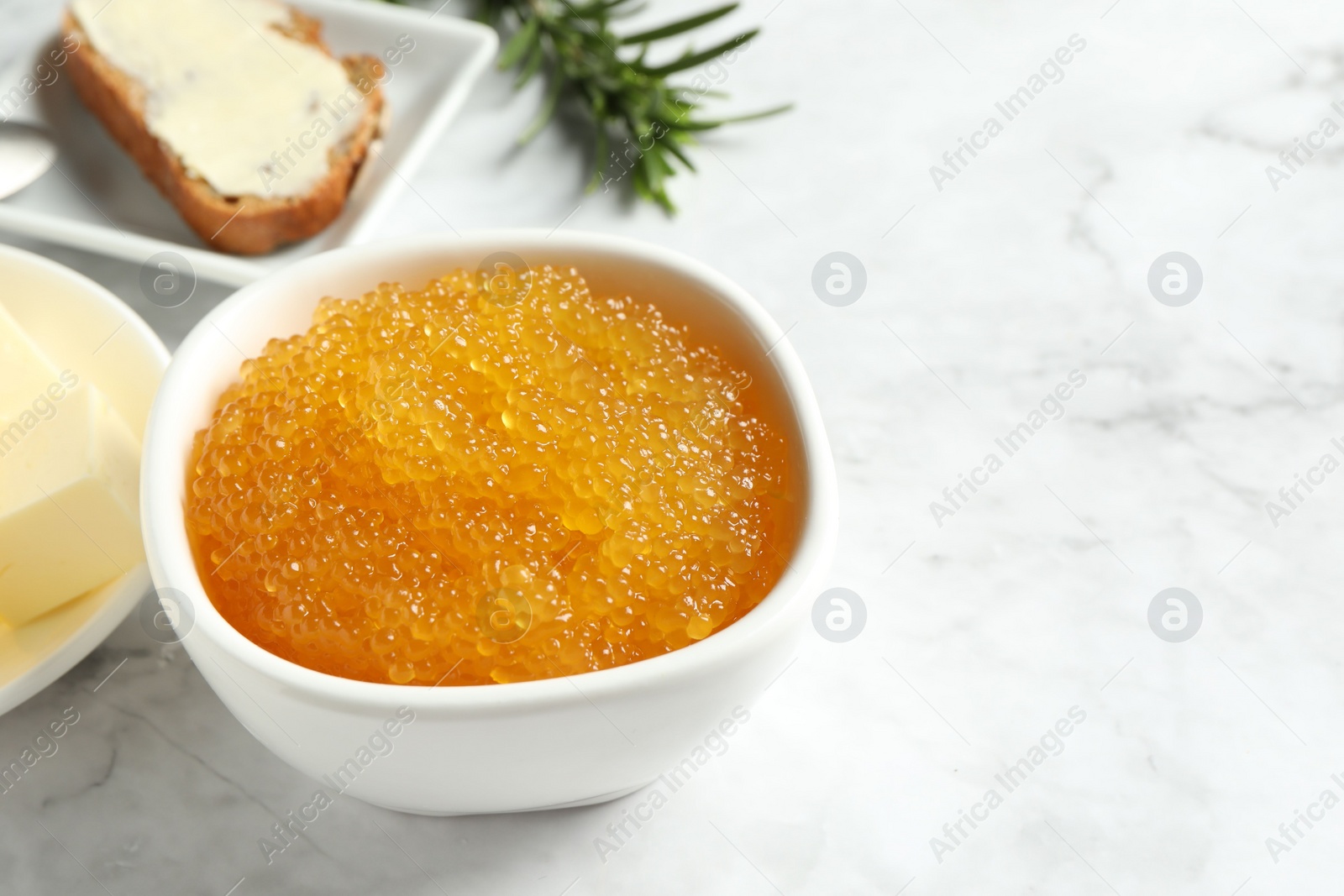 Photo of Fresh pike caviar in bowl, bread, rosemary and butter on white marble table, closeup. Space for text