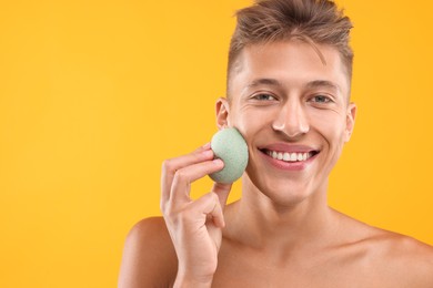 Happy young man washing his face with sponge on orange background. Space for text