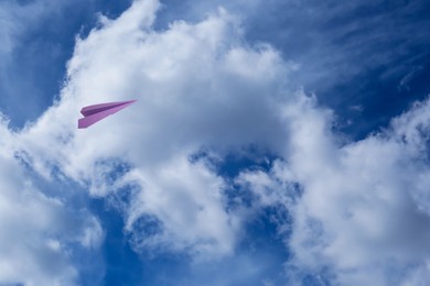 Image of Violet paper plane flying in blue sky with clouds