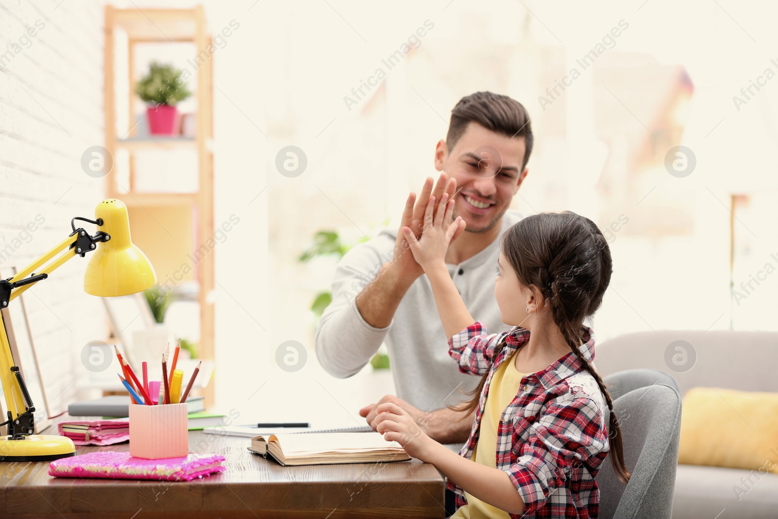 Photo of Father and daughter doing homework together at table indoors