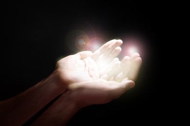 Man stretching hands towards light in darkness, closeup. Praying concept