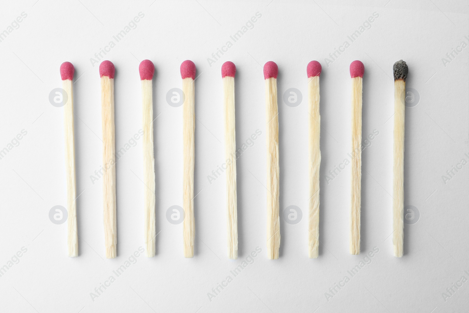 Photo of Row of whole matches and burnt one on white background, top view. Uniqueness concept